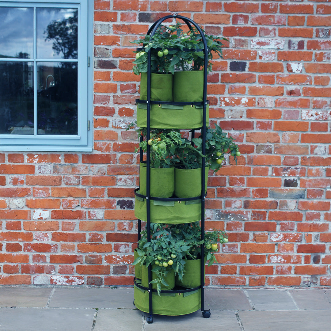 Vigoroot Self Watering Tower Garden with tomato plants in them next to a brick wall